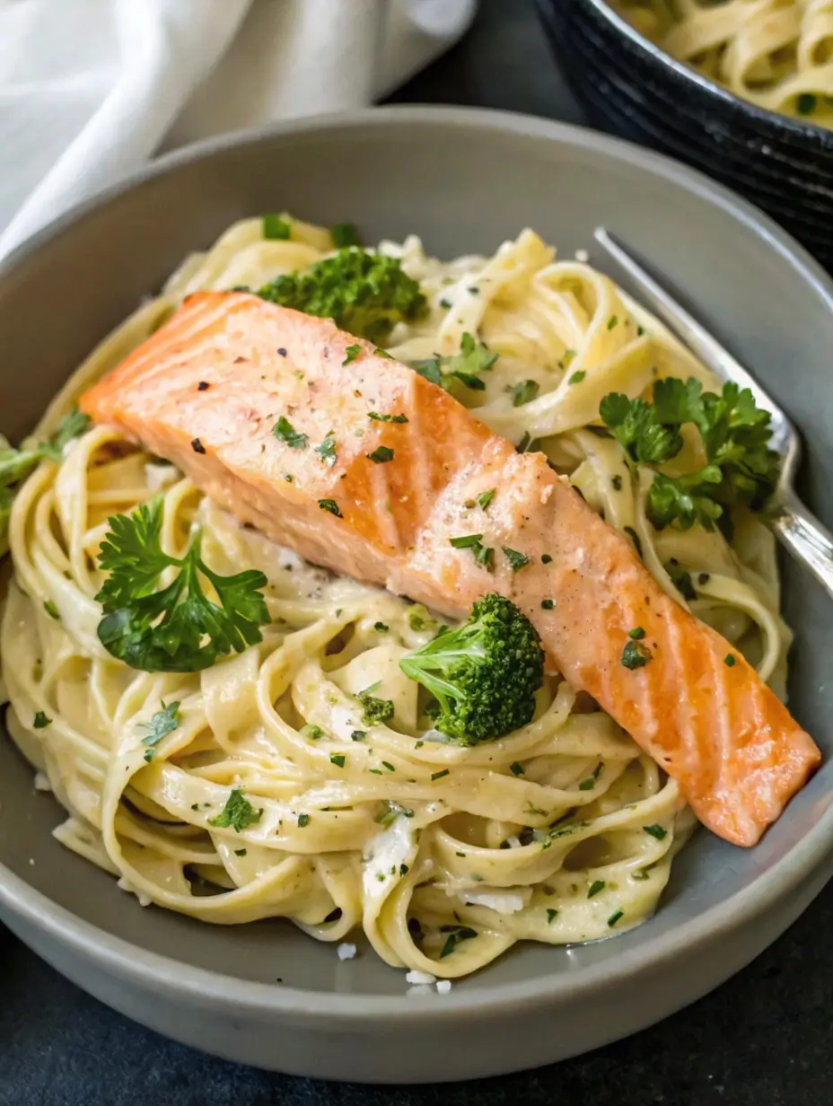 Rich salmon Alfredo pasta served on a white plate with fresh parsley and a touch of lemon zest.