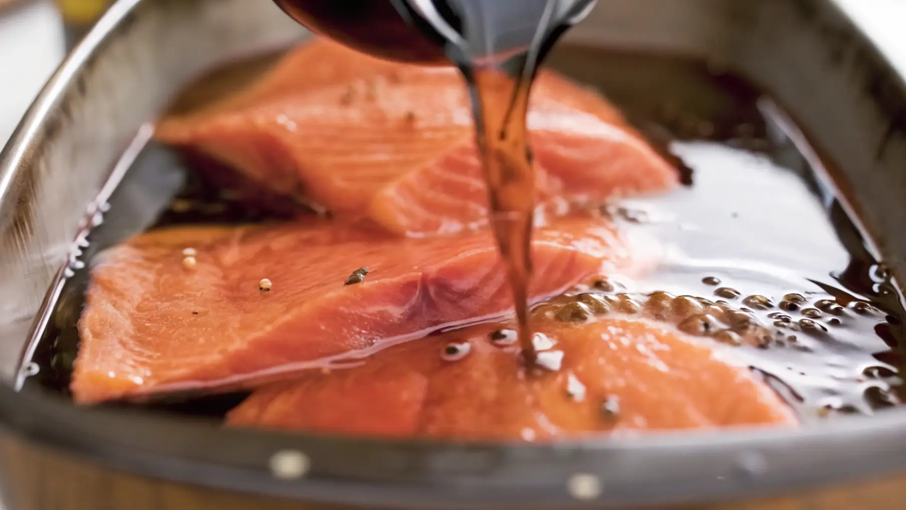 Pouring brine over fresh salmon fillets in a metal pan for smoking preparation.